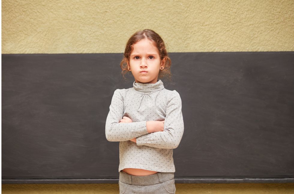 Mädchen im Grundschulalter mit verschränkten Armen und trotzigem Blick