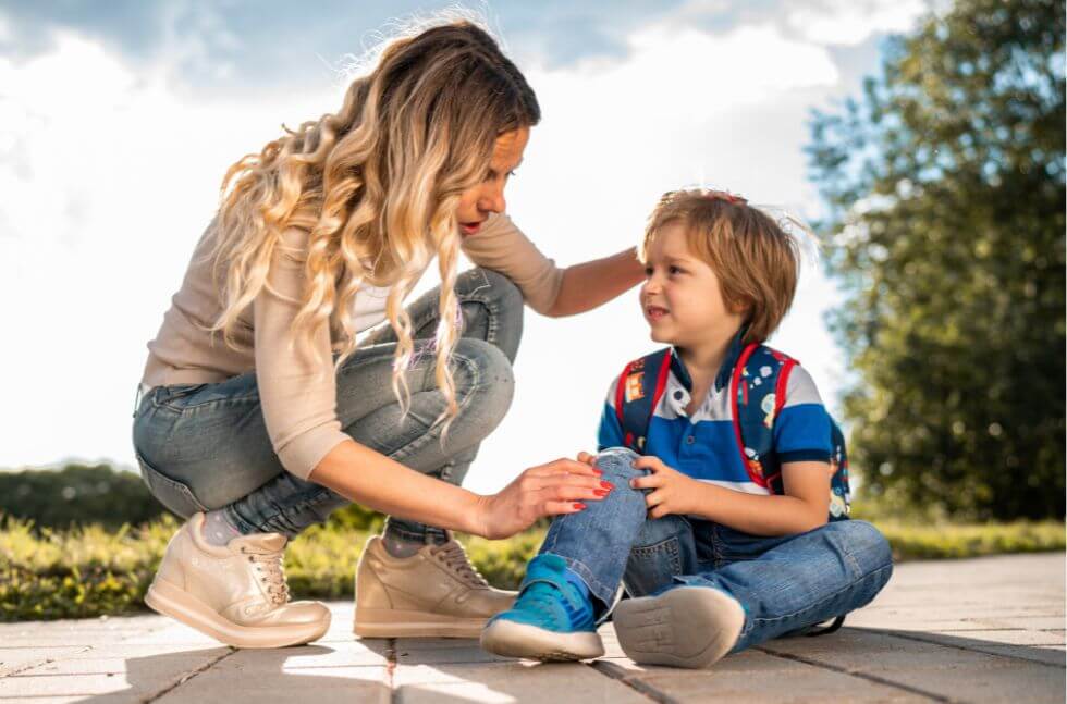 Erzieherin tröstet Kind einfühlsam, das sich beim Sturz leicht verletzt hat