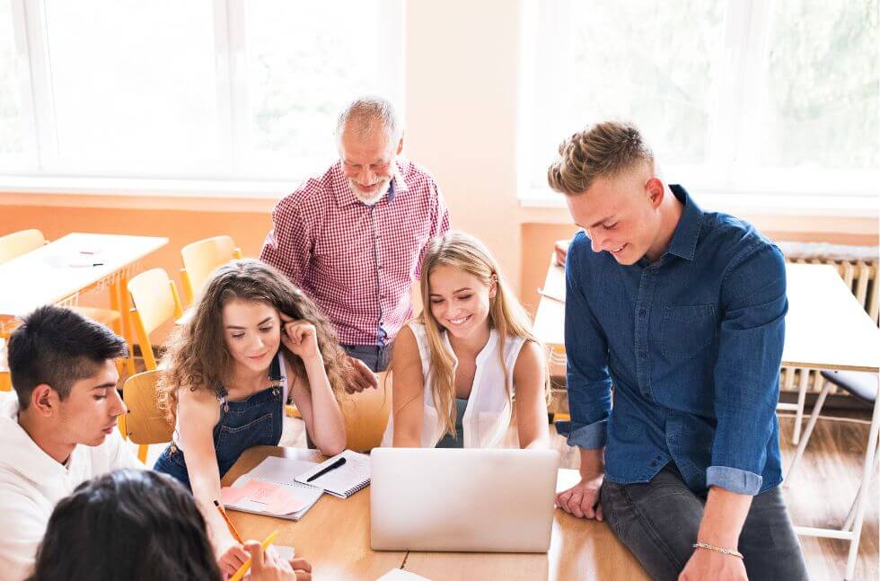 Schüler und Schülerinnen  an weiterführenden Schule bei Gruppenarbeit, Lehrer im Hintergrund 