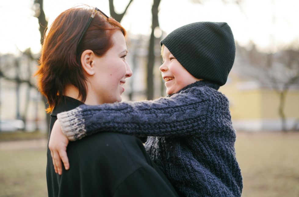 Mutter hält Sohn im Freien im Arm, beide lächeln sich innig an.
