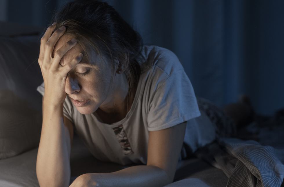 Verzweifelte Mutter liegt nachts auf Bett und fast sich an den Kopf